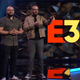 A photo of two men standing on a black-and-blue stage with a large E3 logo behind them.